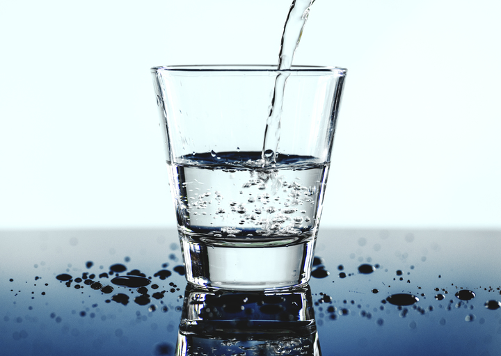 Vaso de agua siendo llenado, con gotas salpicadas alrededor sobre una superficie reflectante.