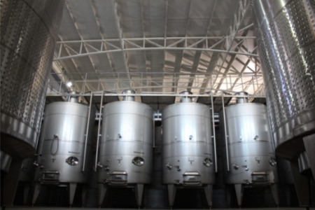 Interior de una bodega con tanques de acero inoxidable utilizados para la fermentación del vino, bajo un techo metálico